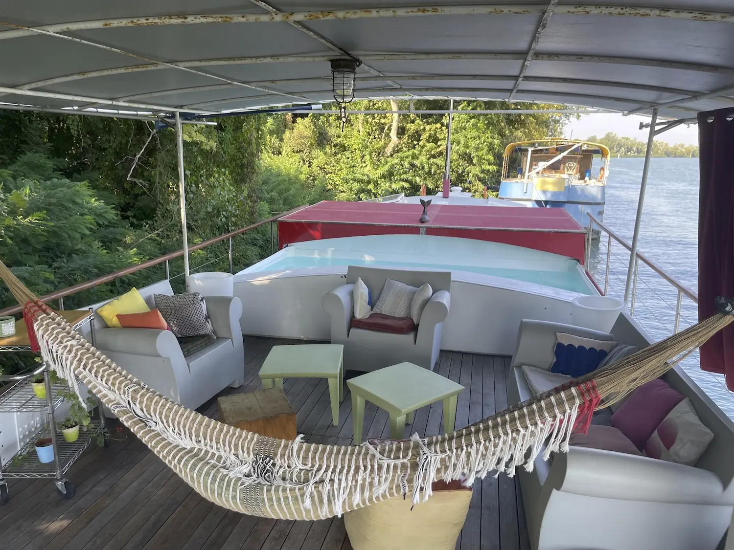photo de la terrasse de la péniche La Paz en été, avec la piscine en eau, le salon d’extérieur et le hamac